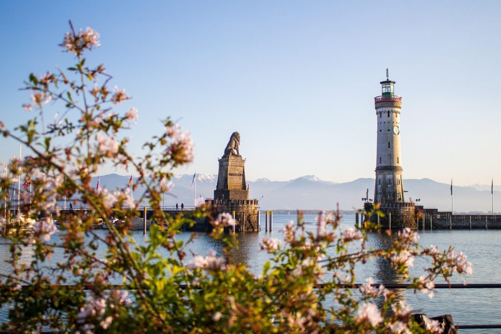 Blick auf eine Hafeneinfahrt am Bodensee. Im Hintergrund sieht man die Berge.